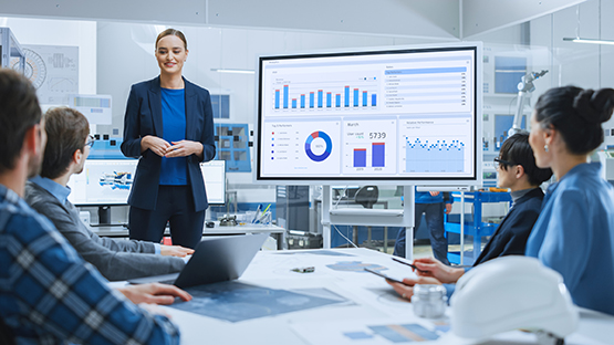 Employee presenting in front of a screen with charts and data
